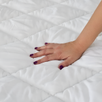 Una mano affonda nell'imbottitura bianca e trapuntata del topper matrimoniale
