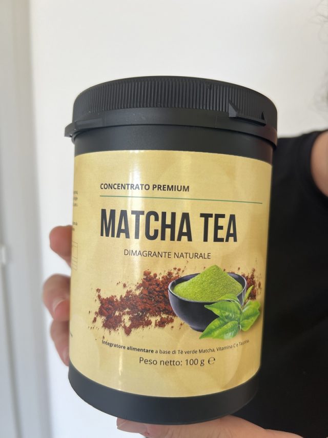 Una mano regge il barattolo di Matcha Tea: tappo nero, etichetta color oro, peso netto 100 g